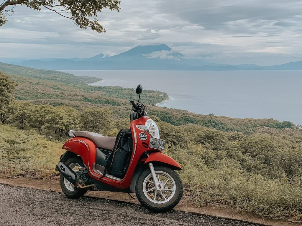 Transport Nusa Penida - A traveler riding a scooter along a coastal road with dramatic cliffs and turquoise water in the background